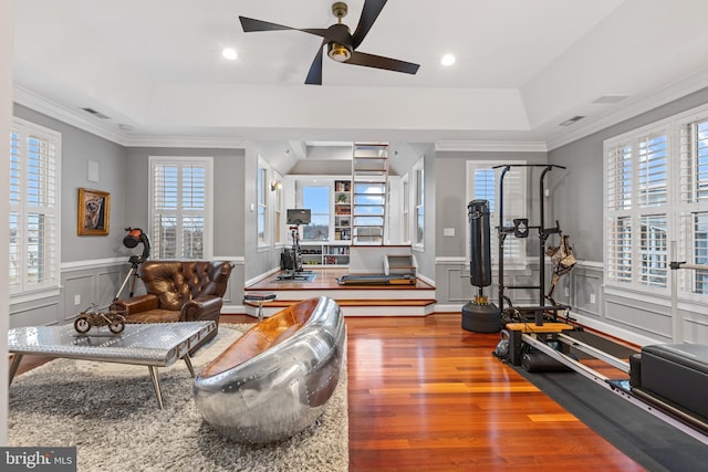 workout area with ornamental molding, a tray ceiling, wainscoting, and wood finished floors