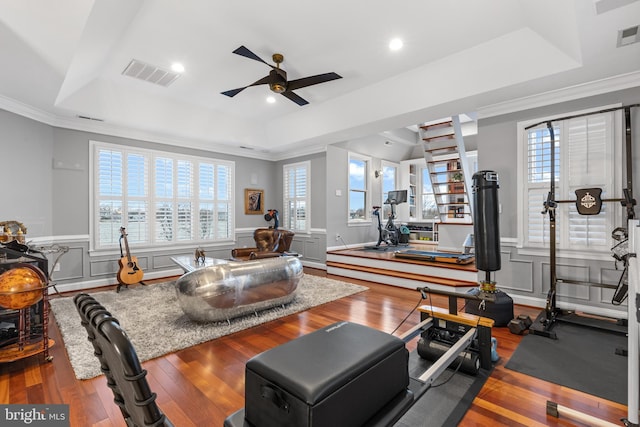 exercise area with a raised ceiling, visible vents, a wainscoted wall, and wood finished floors