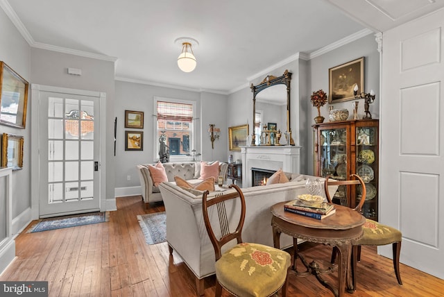 living area with a warm lit fireplace, ornamental molding, wood finished floors, and baseboards