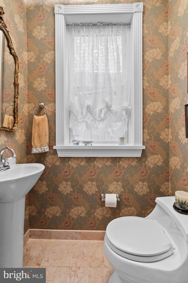 bathroom with baseboards, a sink, toilet, and wallpapered walls