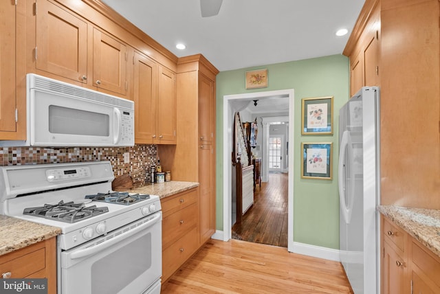 kitchen with light stone countertops, white appliances, light wood-type flooring, and tasteful backsplash