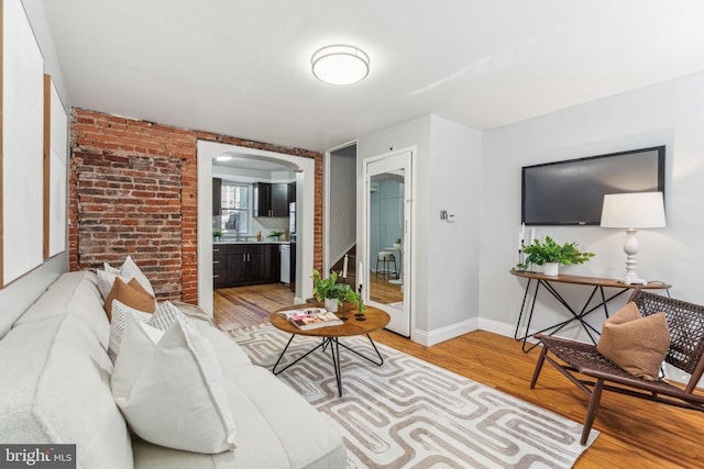 living room with arched walkways, light wood-style flooring, brick wall, and baseboards