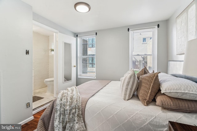 bedroom with multiple windows, ensuite bathroom, baseboards, and wood finished floors