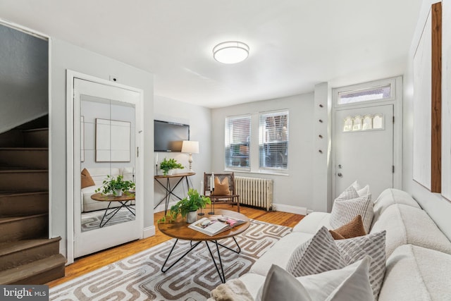 living room featuring stairway, light wood-type flooring, radiator heating unit, and baseboards