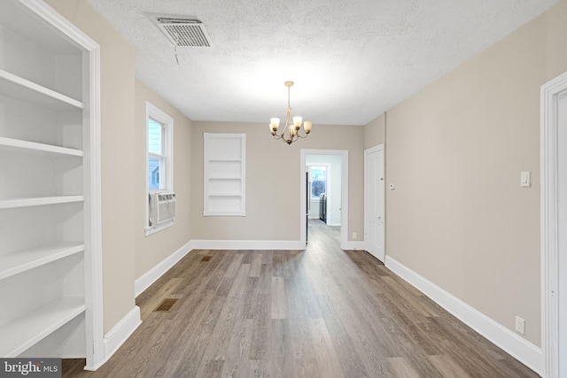 unfurnished dining area with a textured ceiling, a wealth of natural light, wood finished floors, and visible vents