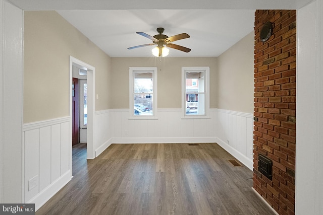 spare room with a wainscoted wall, ceiling fan, dark wood-style flooring, and visible vents