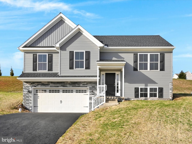 raised ranch featuring a garage, a shingled roof, driveway, board and batten siding, and a front yard