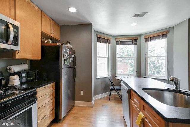 kitchen with stainless steel appliances, a sink, visible vents, light wood finished floors, and dark countertops