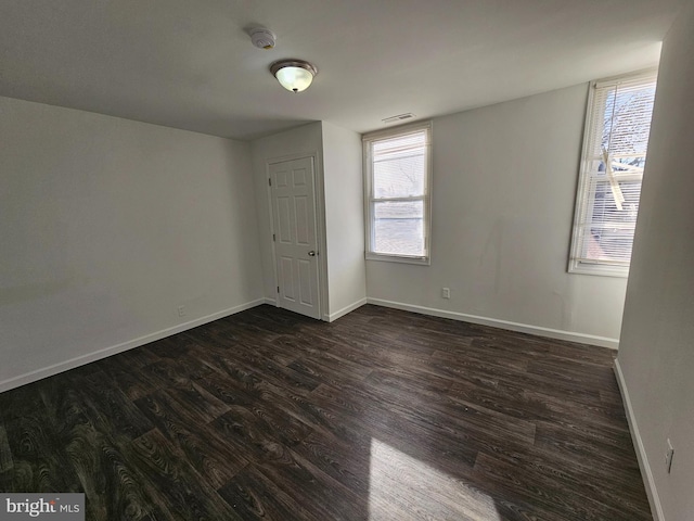 empty room with dark wood-type flooring, visible vents, and baseboards