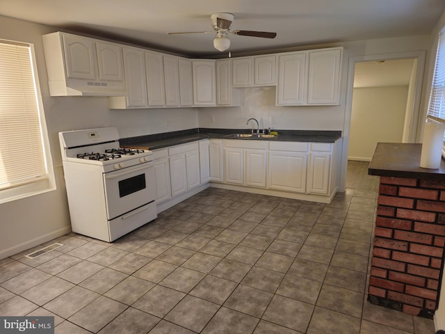 kitchen with dark countertops, visible vents, white cabinetry, white range with gas cooktop, and a sink