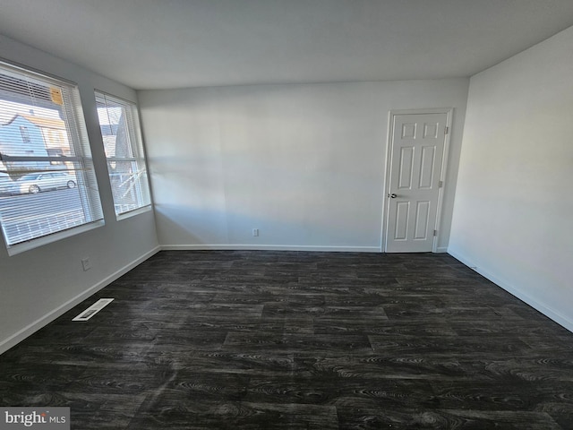 unfurnished room featuring dark wood finished floors, visible vents, and baseboards