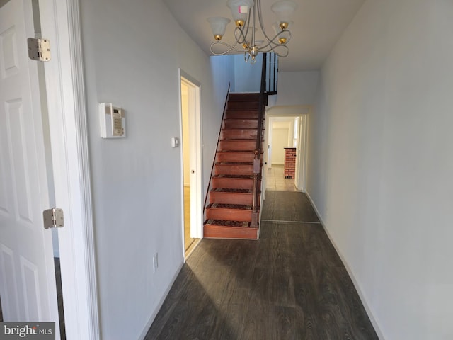 hall featuring stairs, dark wood-type flooring, a chandelier, and baseboards