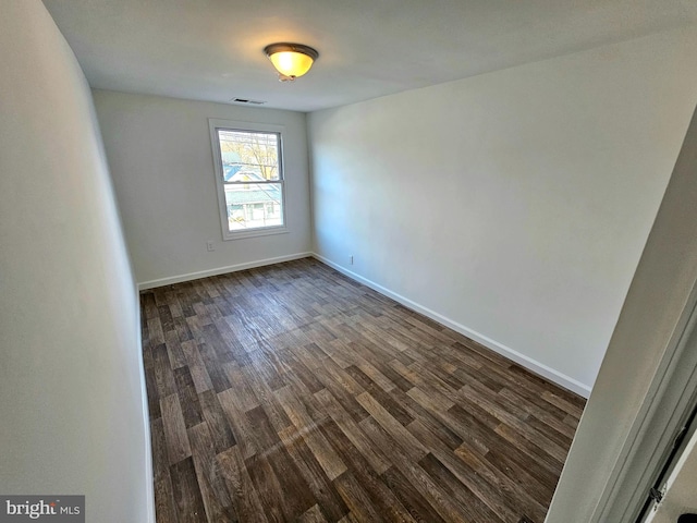 empty room with dark wood-style flooring, visible vents, and baseboards