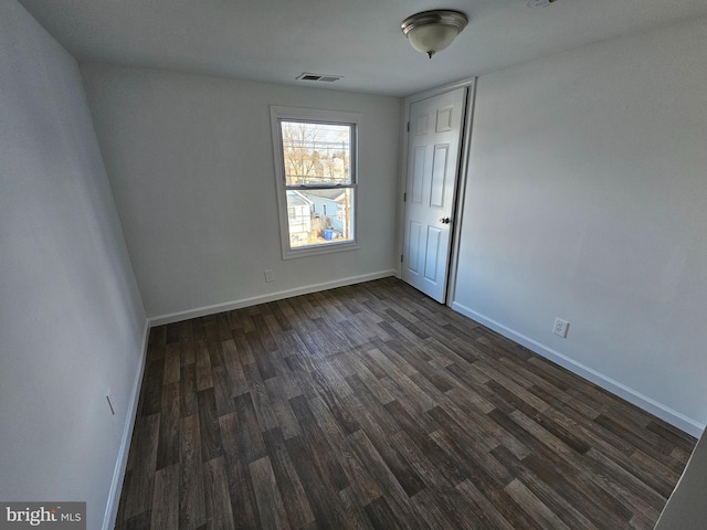 empty room featuring dark wood-type flooring, visible vents, and baseboards