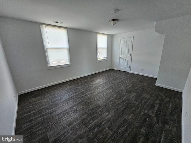 empty room featuring dark wood-style flooring, visible vents, and baseboards