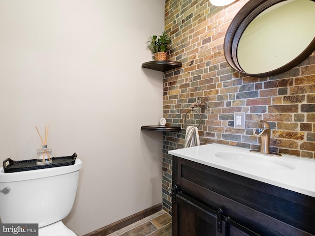 half bath with toilet, brick wall, wood finished floors, vanity, and baseboards