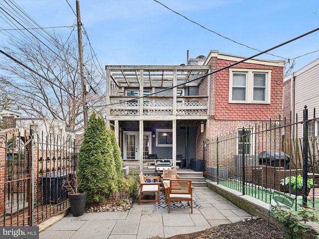 rear view of property with a balcony, a patio area, fence, and brick siding