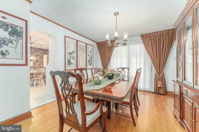 dining room with light wood-style floors, arched walkways, crown molding, and a notable chandelier