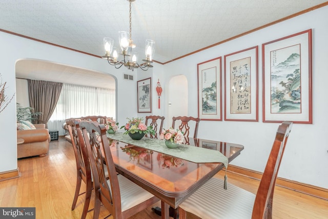 dining room featuring light wood finished floors, visible vents, arched walkways, and ornamental molding