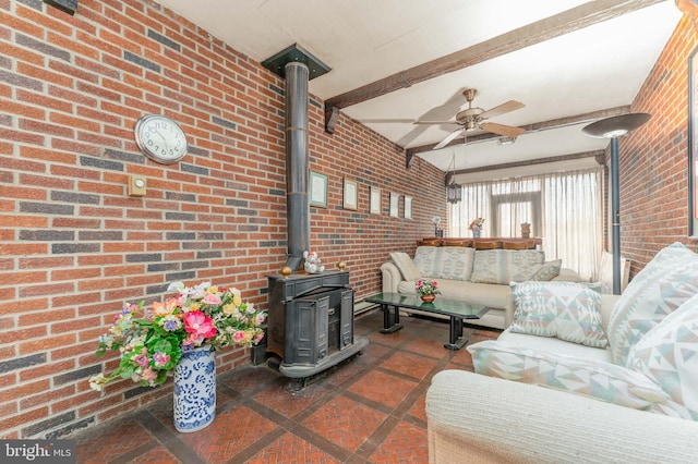 living room with a wood stove, brick wall, ceiling fan, and beamed ceiling