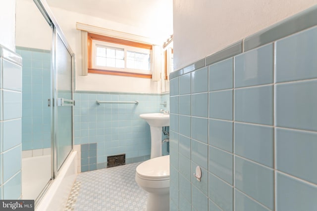 full bath with tile walls, toilet, wainscoting, combined bath / shower with glass door, and tile patterned floors