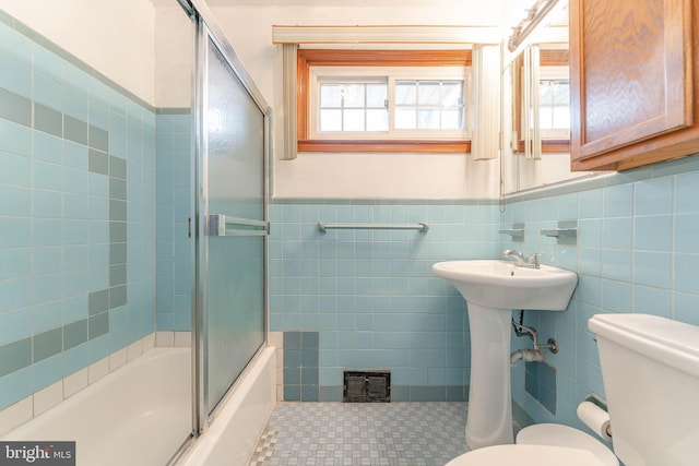 bathroom with tile walls, visible vents, toilet, wainscoting, and combined bath / shower with glass door