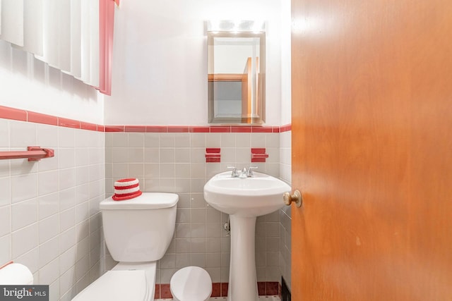 half bath with toilet, a wainscoted wall, and tile walls