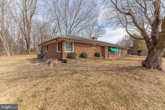 view of front facade with brick siding, a chimney, a front yard, and central air condition unit