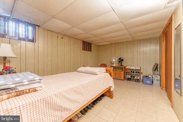 bedroom with a paneled ceiling, wood walls, and tile patterned flooring