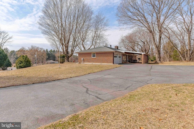 view of side of property featuring brick siding, a chimney, a lawn, a carport, and driveway