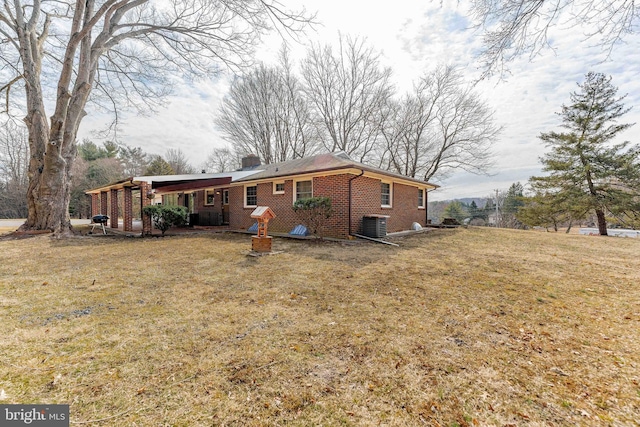 back of property featuring brick siding, a yard, a chimney, and central AC unit