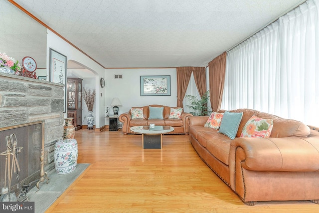 living room with visible vents, arched walkways, light wood-style flooring, ornamental molding, and a stone fireplace