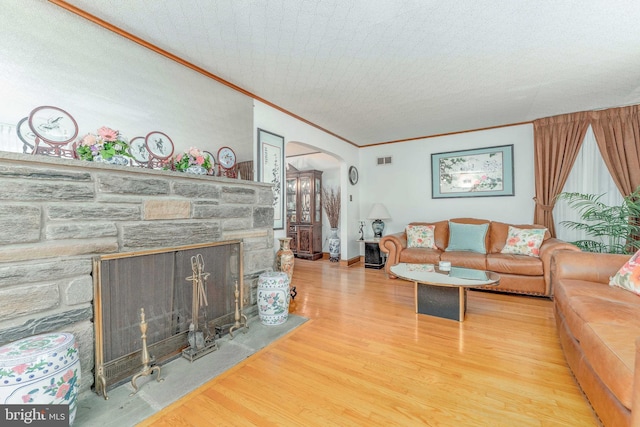 living room featuring arched walkways, a stone fireplace, wood finished floors, visible vents, and ornamental molding