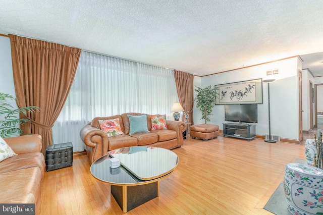 living room with a textured ceiling, wood finished floors, visible vents, baseboards, and crown molding