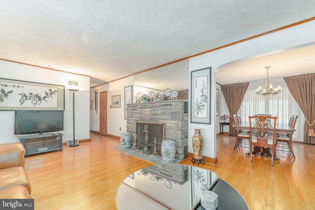 living area featuring an inviting chandelier, a fireplace, ornamental molding, and wood finished floors