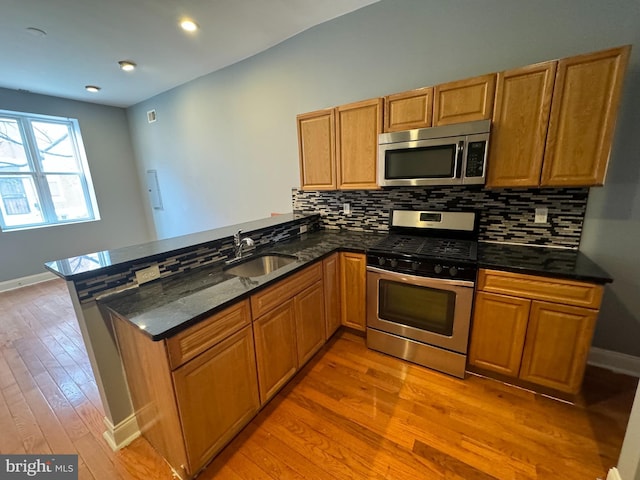 kitchen with appliances with stainless steel finishes, brown cabinetry, a sink, dark stone counters, and a peninsula