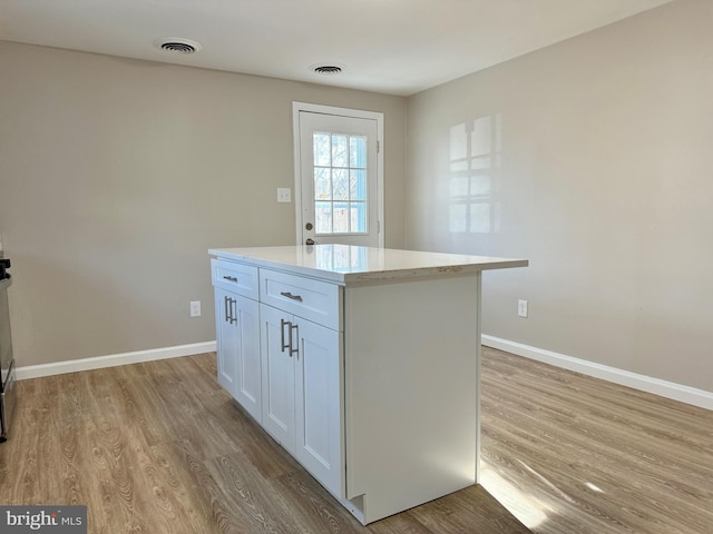 kitchen featuring visible vents, a kitchen island, white cabinetry, and light wood-style flooring