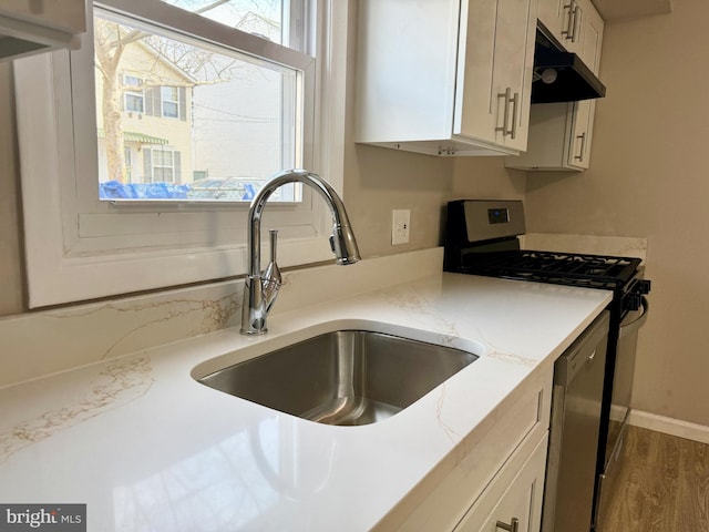 kitchen featuring white cabinets, wood finished floors, stainless steel gas range, under cabinet range hood, and a sink