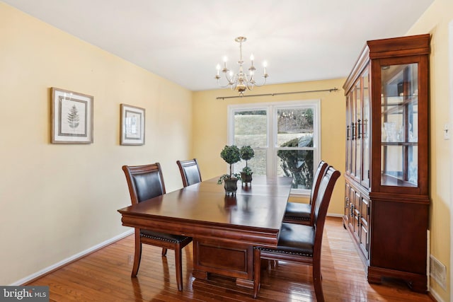 dining room featuring baseboards, visible vents, hardwood / wood-style flooring, and a notable chandelier