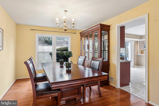 dining area featuring a chandelier, baseboards, visible vents, and light wood-style floors