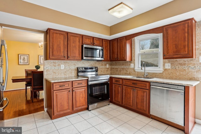 kitchen with appliances with stainless steel finishes, backsplash, a sink, and brown cabinets