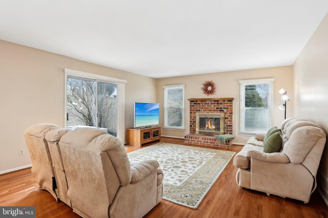 living area featuring a brick fireplace, baseboards, and wood finished floors