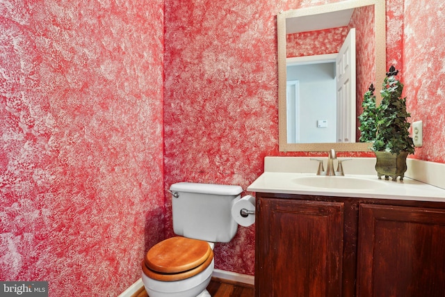 half bathroom with toilet, wallpapered walls, baseboards, and vanity