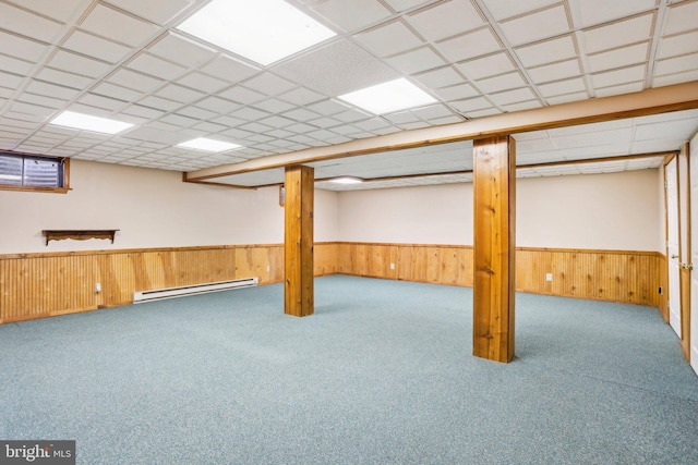 finished basement featuring a baseboard heating unit, wainscoting, a paneled ceiling, and wooden walls