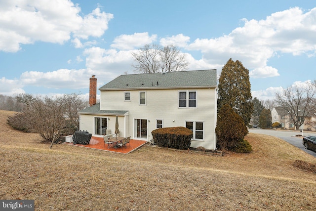 rear view of house featuring a yard, a chimney, and a patio