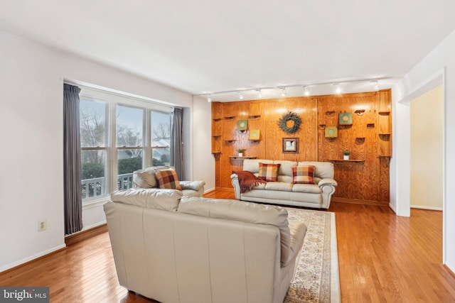 living area with baseboards, wooden walls, and light wood-style floors