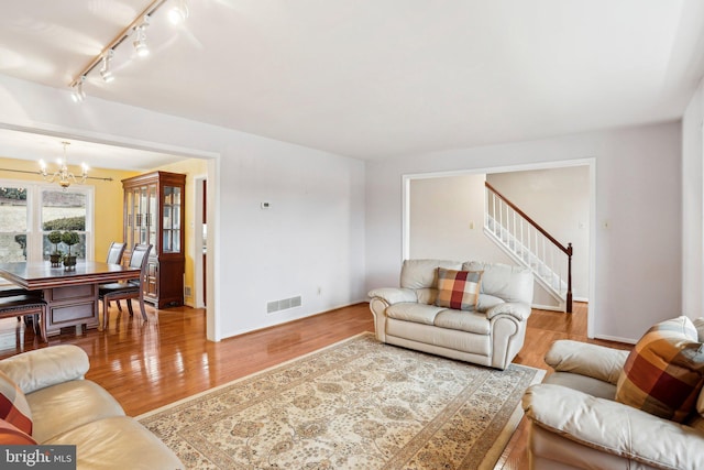 living area with visible vents, wood finished floors, a chandelier, baseboards, and stairs