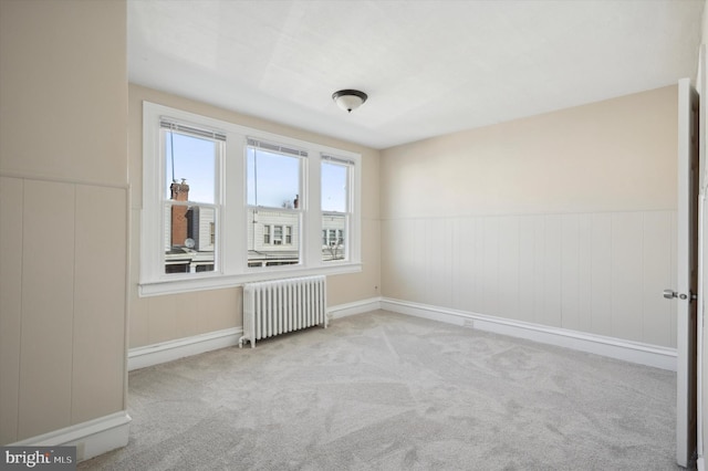 unfurnished room featuring carpet, radiator heating unit, and wainscoting