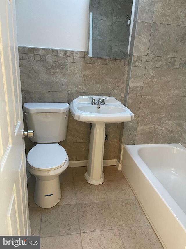 bathroom featuring a sink, tile patterned flooring, toilet, and tile walls