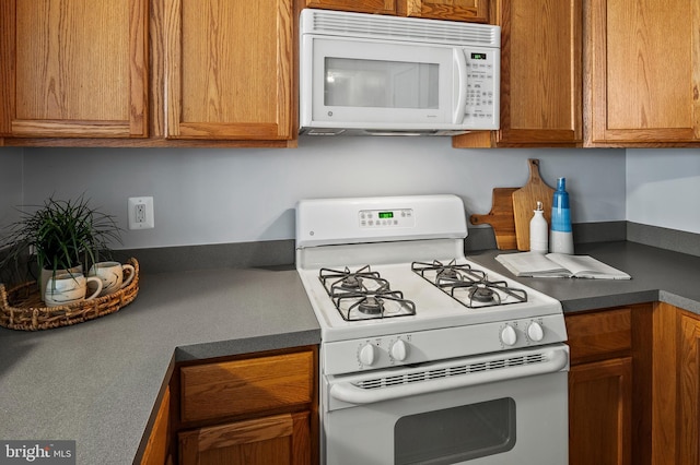 kitchen with dark countertops, white appliances, and brown cabinets